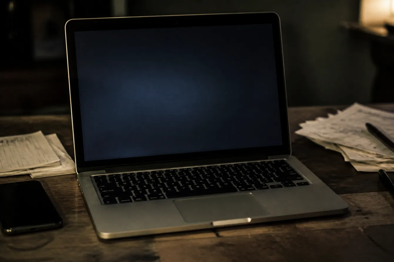 A person examines a .onion address on their laptop, surrounded by notes, in a dimly lit room.